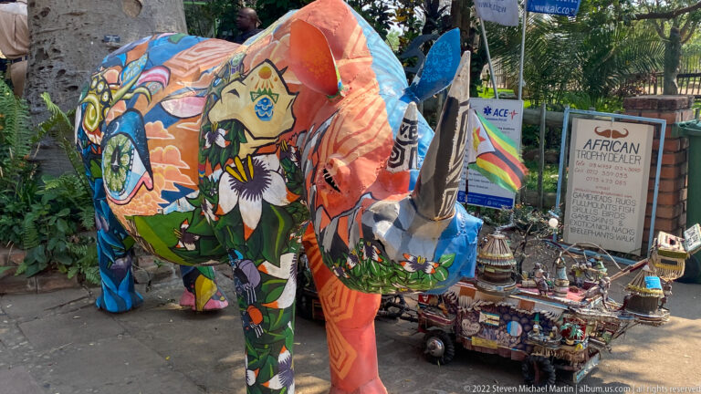 Brightly painted elephant sculptures beside a display of African crafts and a handwritten handicraft sign.