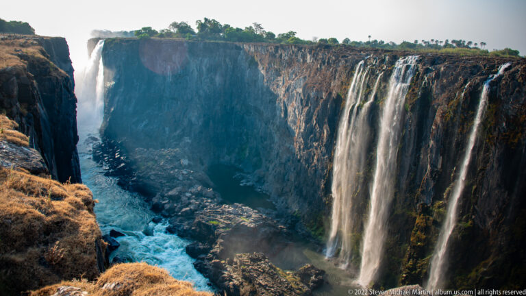 Elevated view into the Victoria Falls gorge with narrow cascades on basalt walls and blue-white river rapids flowing through the canyon.