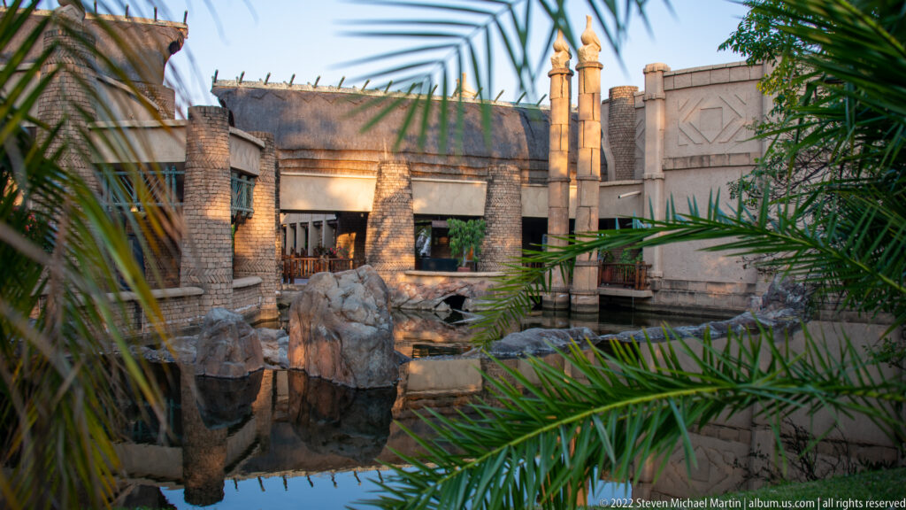 Courtyard of The Victoria Falls Hotel with pale masonry, palms, arched openings, and a rock-edged water feature.