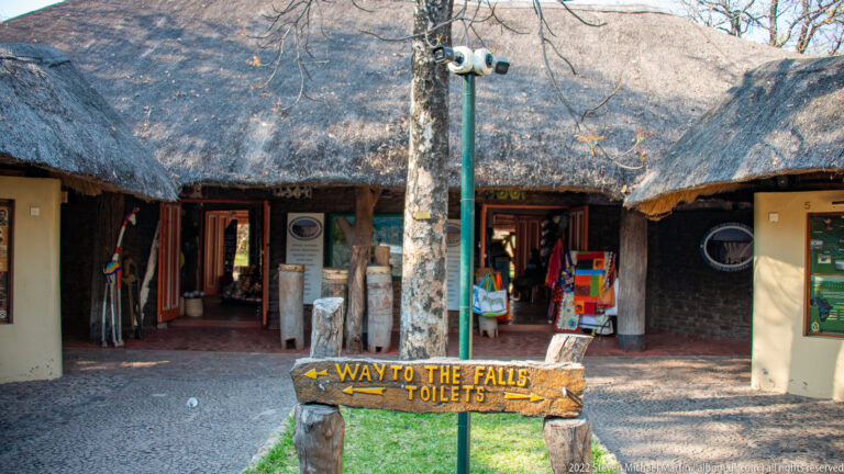Thatched visitor building with open doorways and a wooden arrow pointing toward the falls and toilets.