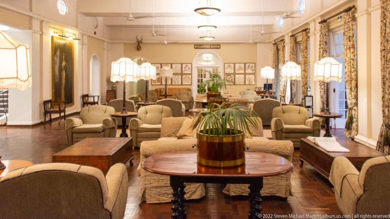 Wide view of Stanley's Room with cream seating, dark wood tables, lamps, botanical prints, curtains, and polished floor.