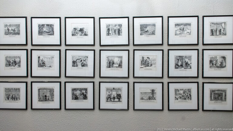 Multiple small framed black-and-white historical prints arranged in a regular grid on a pale wall.