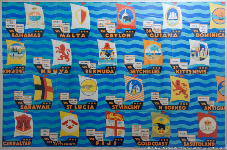 Blue display panel with historic colonial flags, territory names, and small labels identifying traded goods.