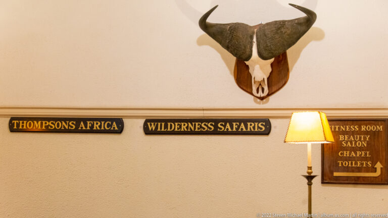 Horned bovine skull mounted above signs for safari companies and directions to hotel facilities.