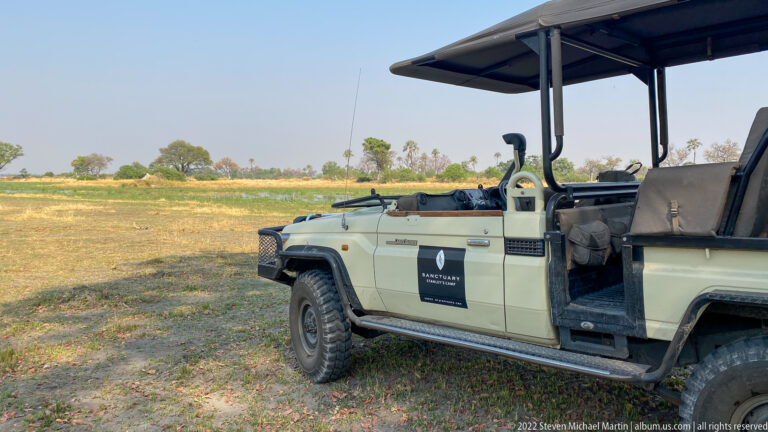 Open-sided safari vehicle with raised seats and canvas roof parked beside a broad grassy floodplain.