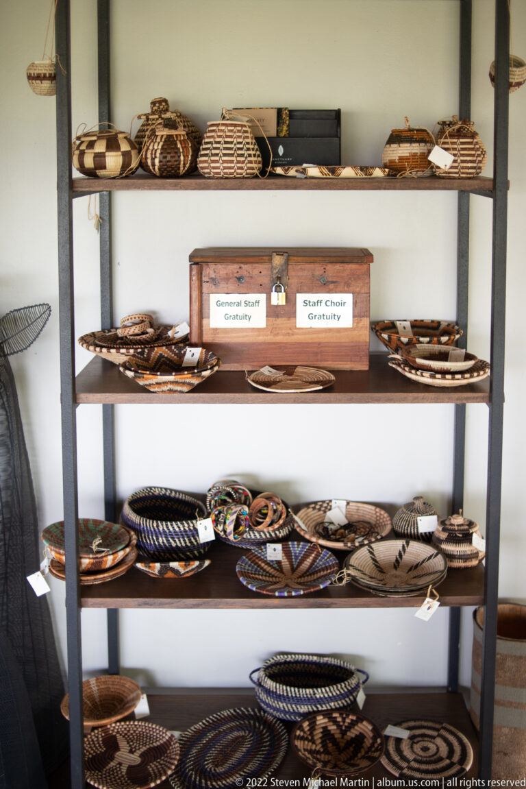 Shelves filled with patterned woven baskets, trays, beadwork, and other handmade craft objects in a safari lodge.