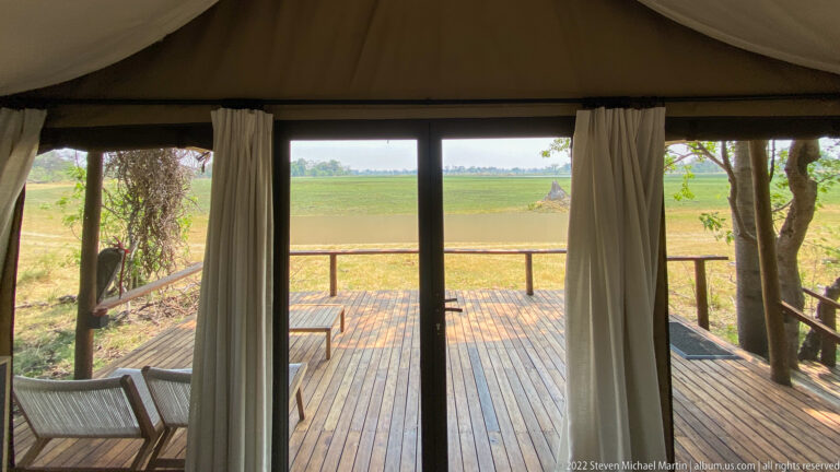 View through glass doors onto a private wooden deck with lounge chairs overlooking a broad green floodplain.