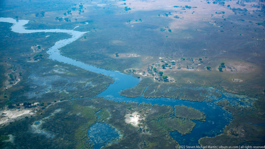 Aerial view of a broad blue channel bordered by green marsh, small pools, islands, and drier floodplain.