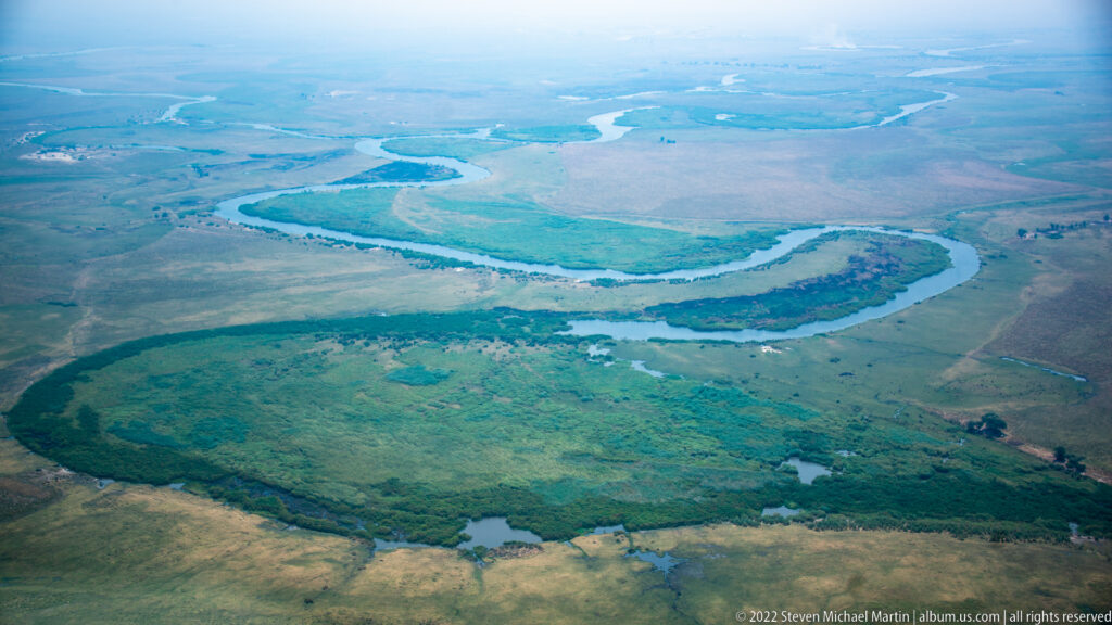 Aerial view of winding blue channels, green floodplain vegetation, and scattered pools across the Okavango Delta.