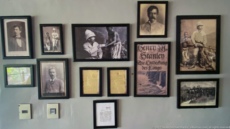 Wall display of framed historical portraits, documents, expedition photographs, and a Henry Morton Stanley-themed print.