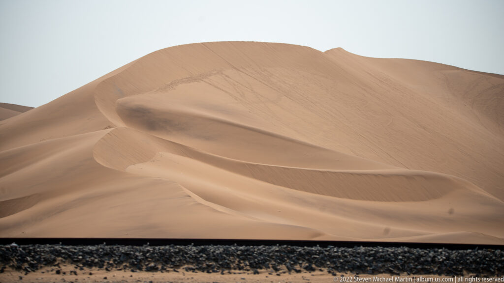 Close view of a pale orange dune with sweeping crests and slip faces above a dark gravel strip.