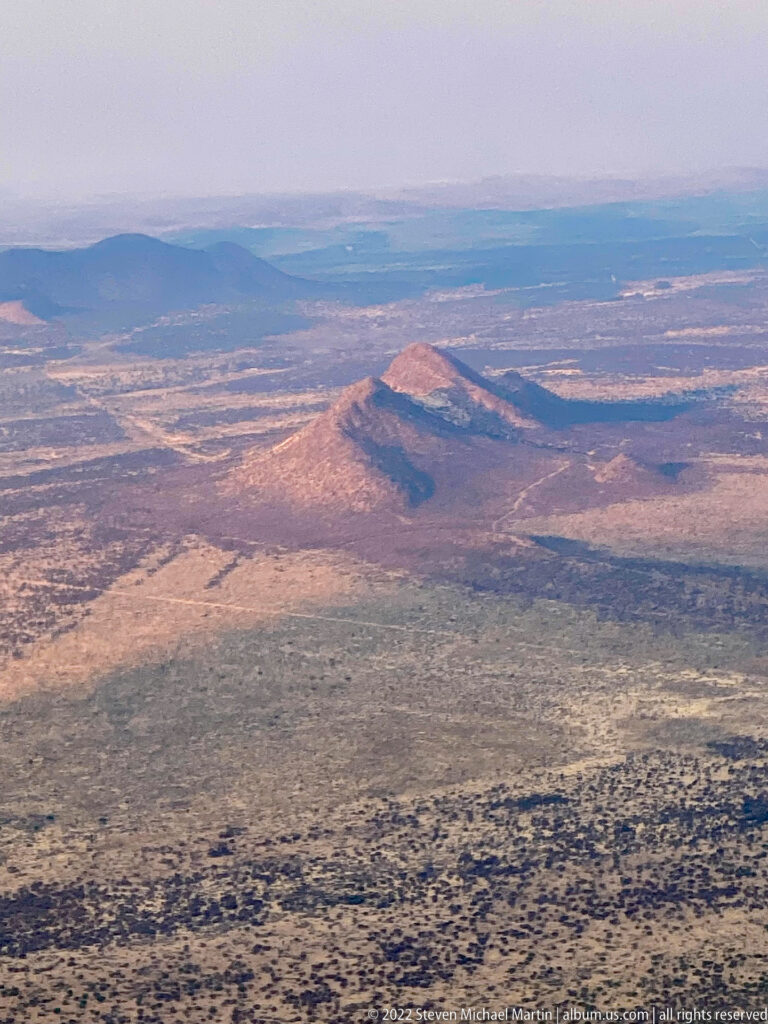 Aerial view of isolated rounded rocky hills casting shadows across an arid plain with sparse vegetation.
