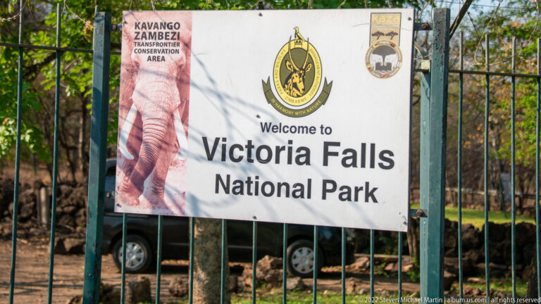 Banner on a metal gate reading Welcome to Victoria Falls National Park, with park and conservation logos.
