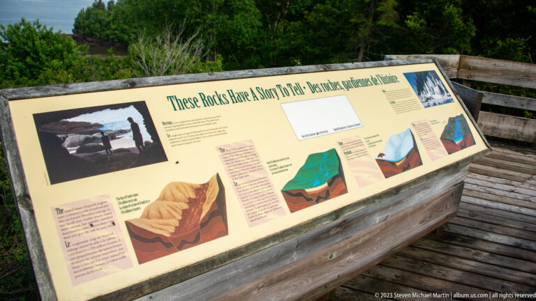 Geology panel titled These Rocks Have a Story To Tell with diagrams on a wooden coastal overlook.