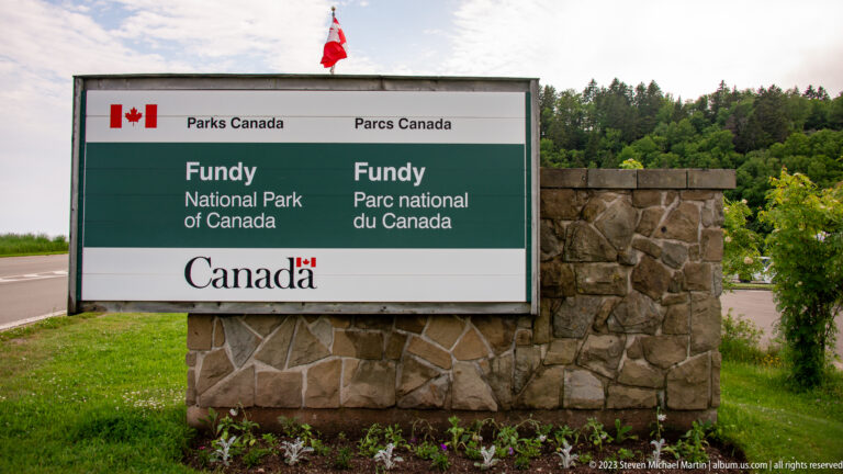 Bilingual Fundy National Park of Canada sign on a stone base beside the road, with Canadian flag above.