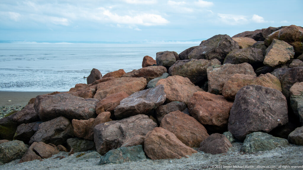 Large angular riprap boulders piled beside exposed tidal flats and the Bay of Fundy.