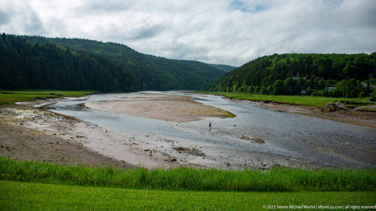 Narrow tidal channel winding through broad exposed flats between forested hills near Alma.