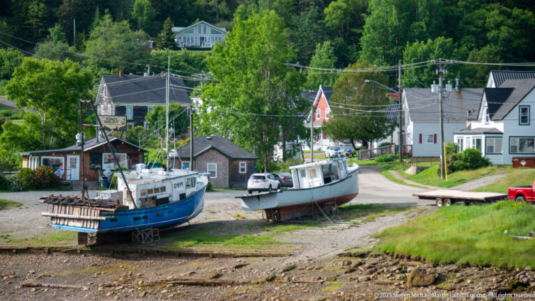 Fishing boats grounded on the exposed harbor bottom at low tide beside houses and waterfront buildings in Alma.