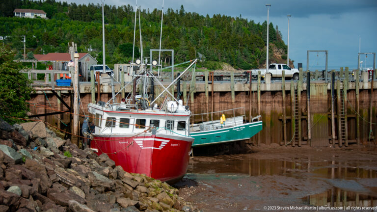 Red and green fishing boats grounded below a high timber wharf at low tide in Alma.