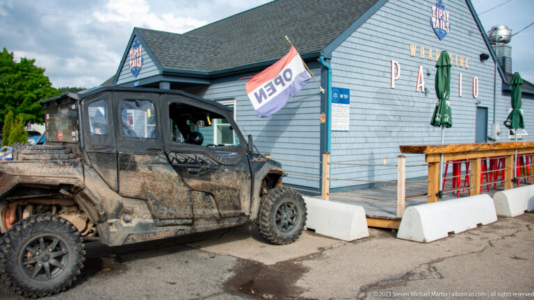 Muddy off-road vehicle parked beside a gray visitor-area building with an OPEN flag near Hopewell Rocks.