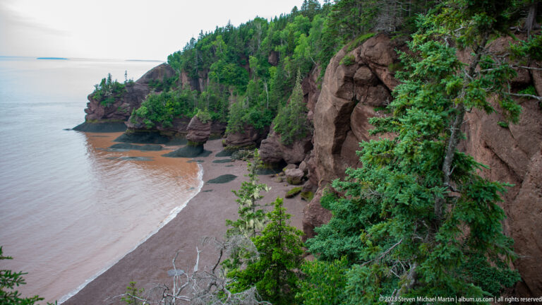 Wide overlook of Hopewell Rocks cliffs, sea stacks, exposed tidal flats, and calm Bay of Fundy water.