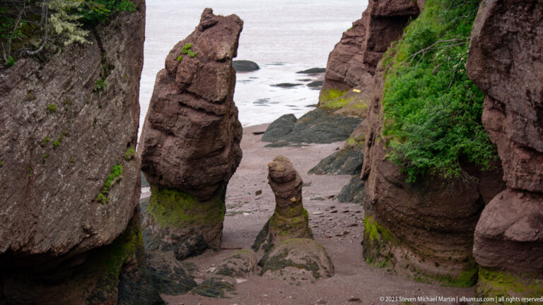 Slender reddish Hopewell Rocks pillars standing between cliff walls on the exposed seabed at low tide.