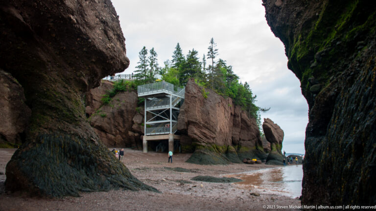 Gray Hopewell Rocks access tower rising between cliffs above visitors walking on the exposed shore.
