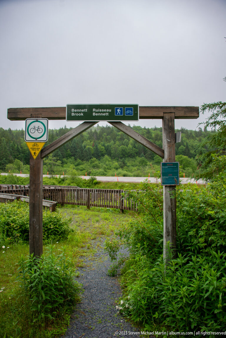 Timber trailhead gateway over a gravel path leading into dense vegetation at Bennett Brook.