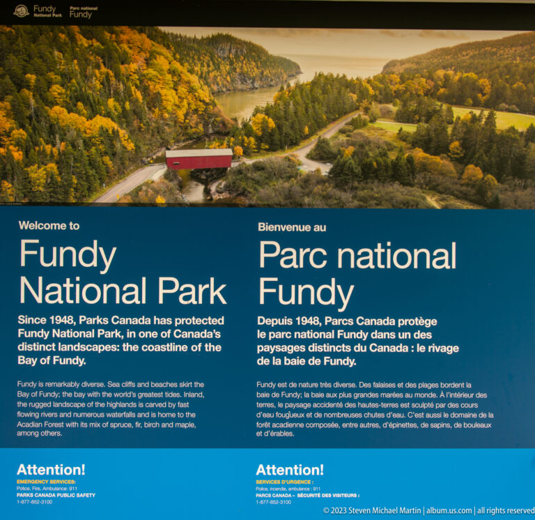 Bilingual Welcome to Fundy National Park panel beneath an autumn landscape photograph with a red covered bridge.