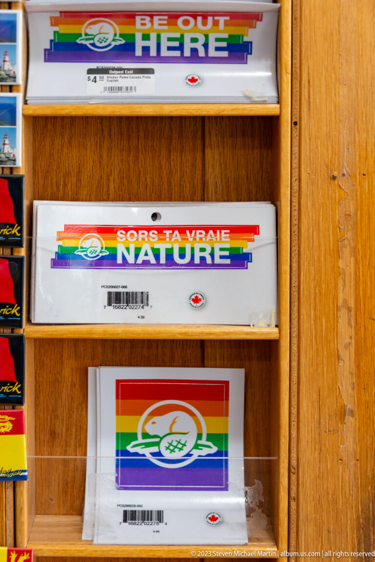 Rainbow-striped Parks Canada merchandise and bilingual pride-themed items displayed on a wooden gift-shop rack.