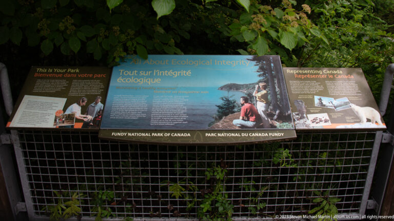 Bilingual ecological-integrity interpretive panels mounted against dense vegetation in Fundy National Park.