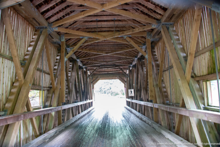 Centered view through Point Wolfe covered bridge showing repeated timber trusses and a bright far portal.