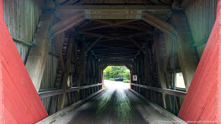 Red portal framing the dark timber interior and bright far opening of Point Wolfe covered bridge.