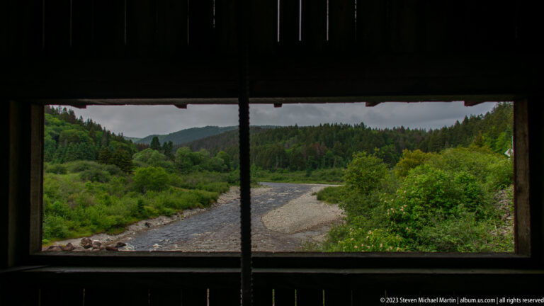 Point Wolfe River and gravel bar framed by a dark rectangular opening in the covered bridge.