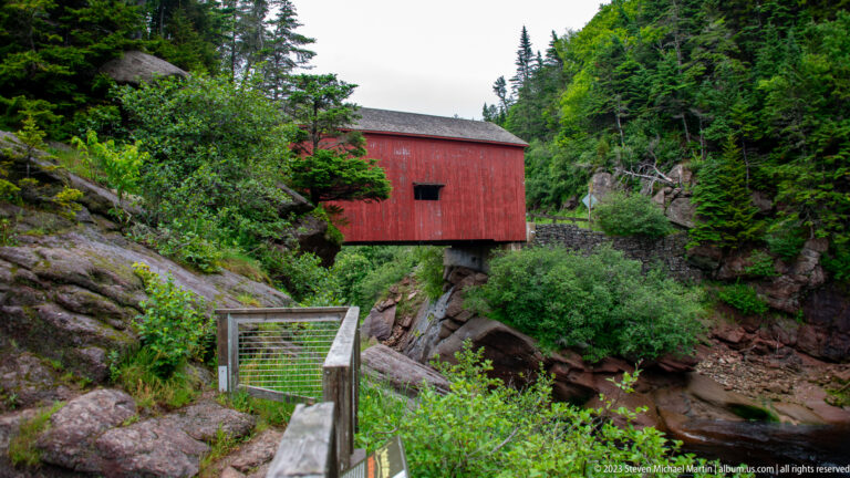 Red Point Wolfe covered bridge crossing a rocky forest gorge beyond a pedestrian railing.