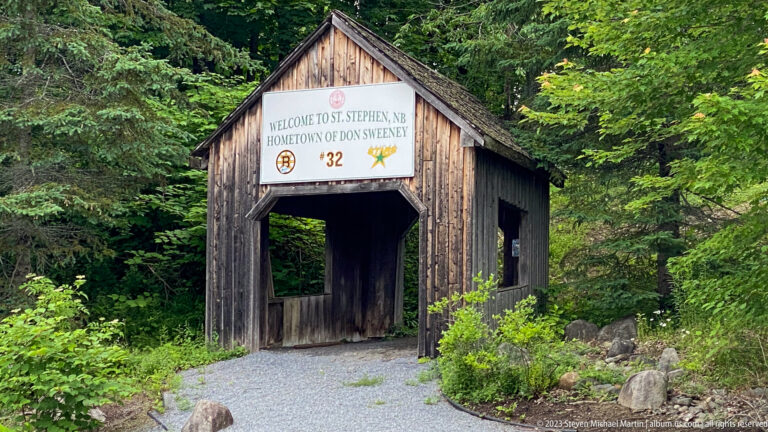 Small rustic covered bridge in trees with a welcome sign for St. Stephen, New Brunswick.