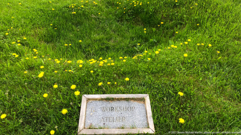 Rectangular stone marker reading Workshop and Atelier set in lush grass dotted with yellow wildflowers.