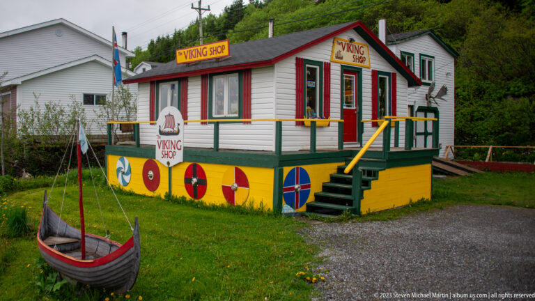 Colorful building labeled Viking Shop with painted shield motifs, porch, and a small Norse-style boat replica on the lawn.