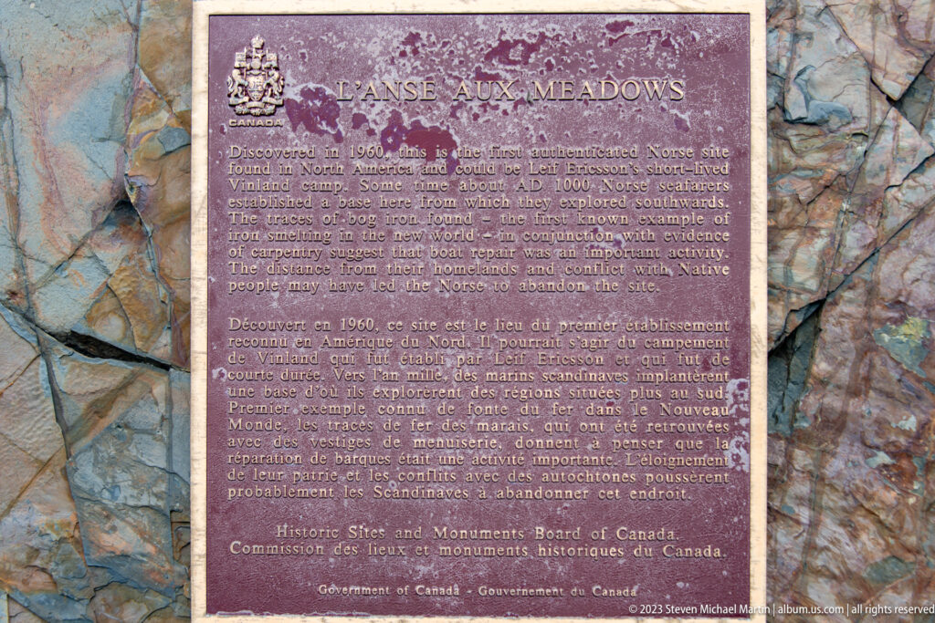 Weathered bilingual commemorative plaque titled “L’Anse aux Meadows,” mounted against a rough stone background.