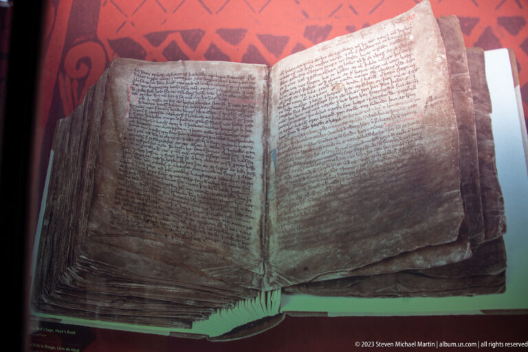 Close view of an open medieval manuscript with dense script, worn pages, and red decorative elements.