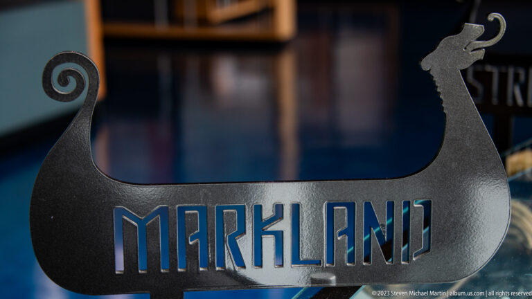 Black Viking longship-shaped metal display with curled stern, animal-headed prow, and cut-out word “MARKLAND.”