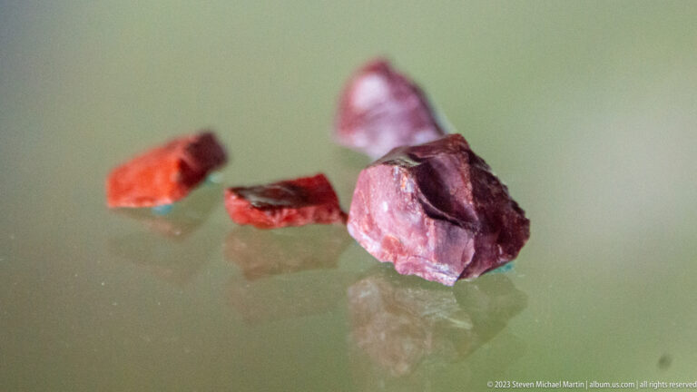 Several irregular red and purple stone fragments arranged on a reflective display surface.