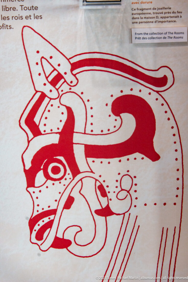 Red interpretive line drawing of a stylized interlaced animal with curling body and ribbon-like ornament.