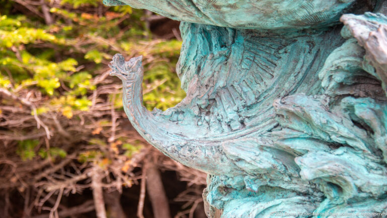 Close view of textured blue-green patinated bronze sculpture with ridged surfaces and a small upright projection.