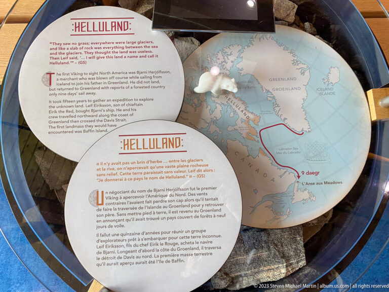Circular Helluland interpretive map with red route between Greenland and the Canadian Arctic, accompanied by bilingual text.
