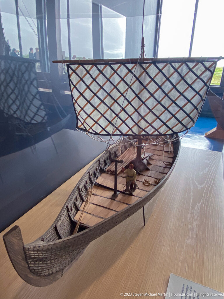 Detailed wooden model of a Norse sailing vessel with lattice-pattern square sail, mast, clinker hull, and deck fittings.