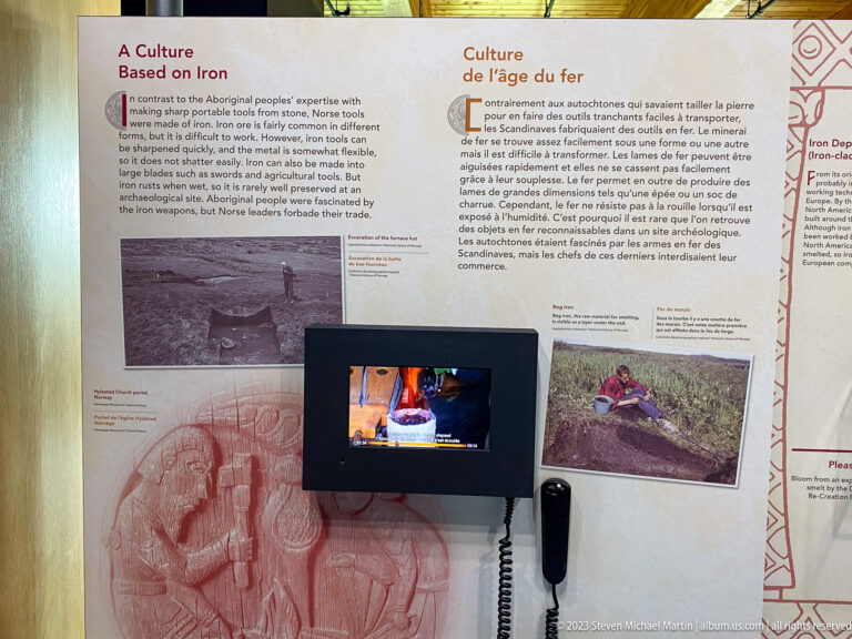 Bilingual ironworking exhibit with photographs, technical illustration, explanatory text, and a small video monitor showing a fire.