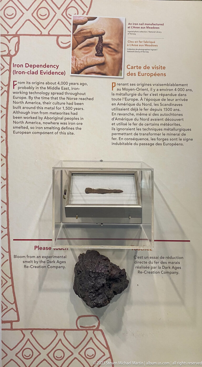 Two archaeological iron objects in clear display cases, including a slender piece above and a corroded dark mass below.