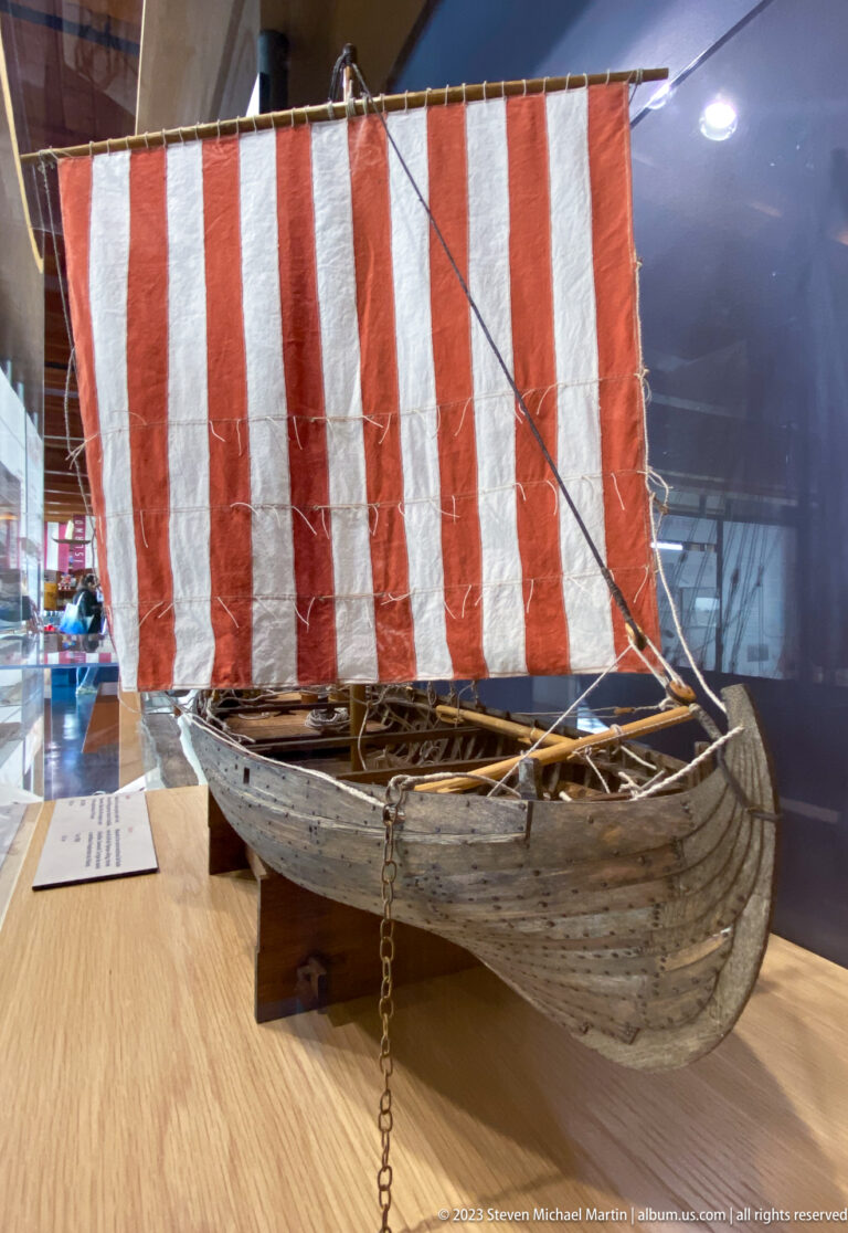 Wooden Norse-style ship model with curved clinker-built hull, rigging, and a red-and-white striped square sail.