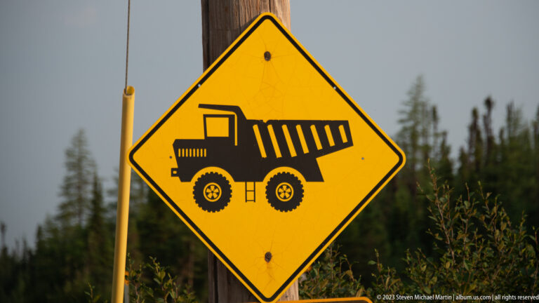 Yellow diamond road sign with black silhouette of a large off-highway mining dump truck.